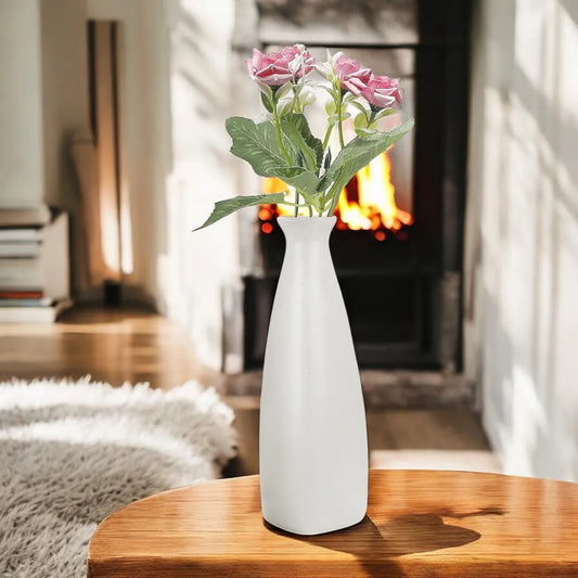 White ceramic triangular bottle vase with pink flowers, minimalist home décor accent in a cozy living room setting.