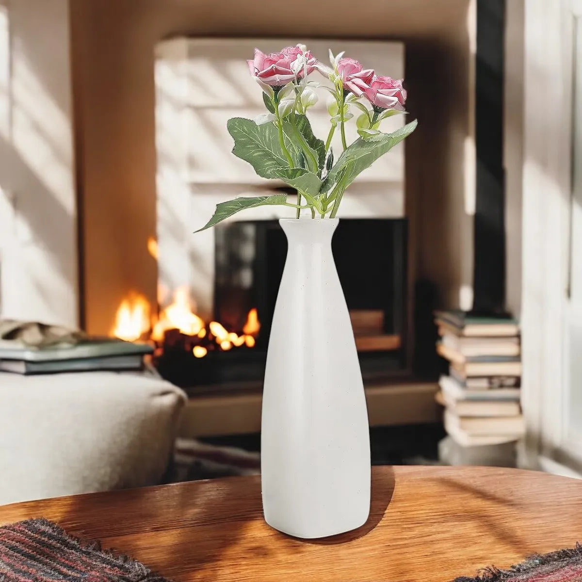 White ceramic triangular bottle vase with pink flowers on a wooden table in a cozy living room.