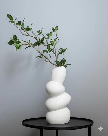 White ceramic wave flower vase on a black table, featuring green leaves for minimalist décor.