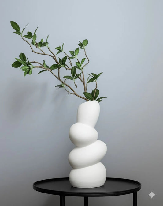 White ceramic wave flower vase on a black table, featuring green leaves for minimalist décor.