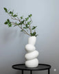 White ceramic wave flower vase on a black table, featuring green leaves for minimalist décor.
