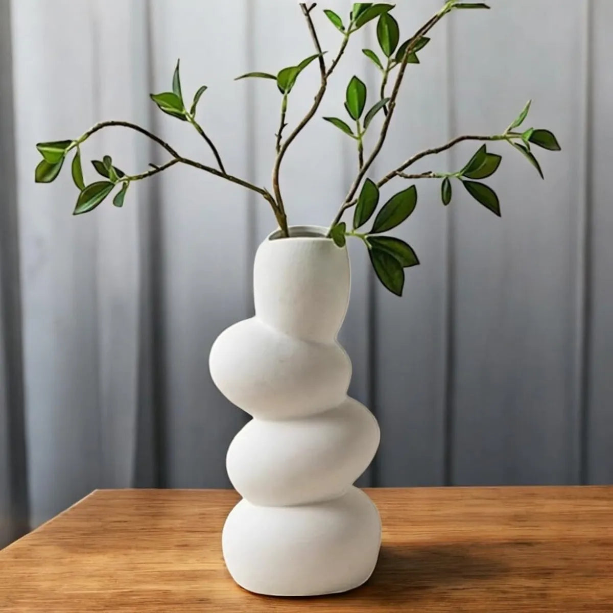 Aesthetic white ceramic wave flower vase featuring a sculptural design with green branches.