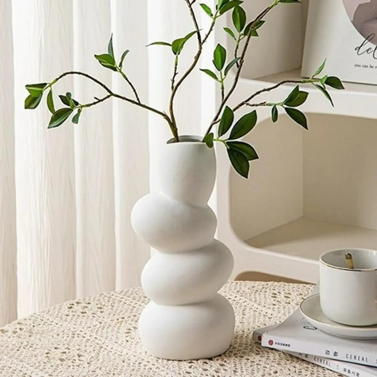 White ceramic wave flower vase with greenery, showcasing a minimalist and sculptural design in a stylish setting.